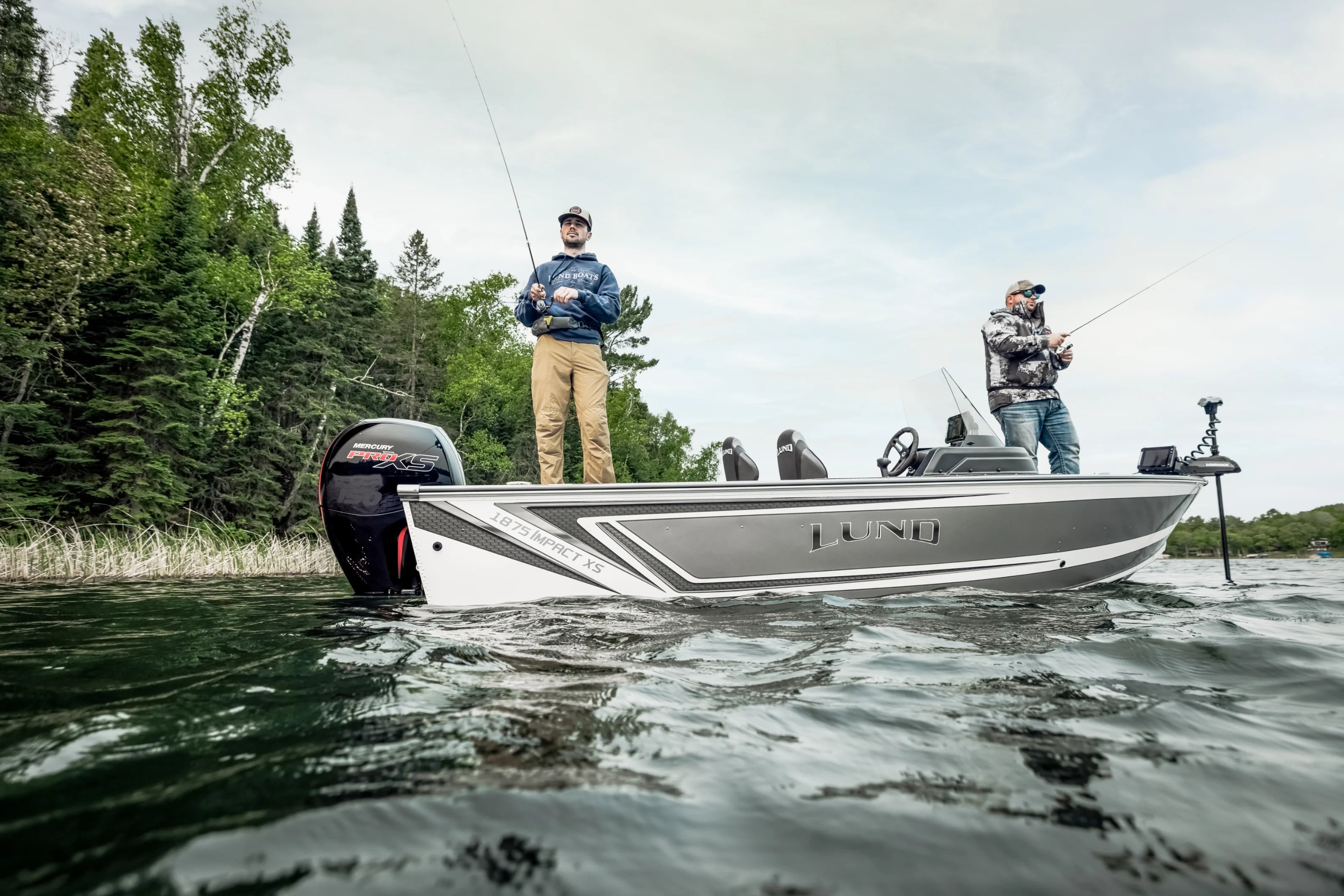 Two people fishing from a Lund boat on a lake with trees in the background